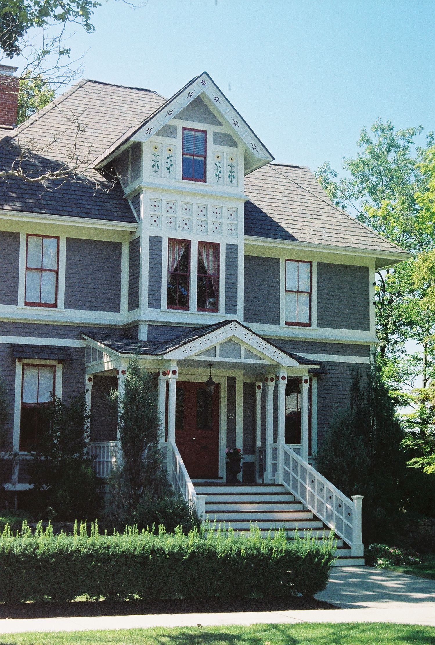 Two-story Victorian house with gray siding, white trim, and a red front door.