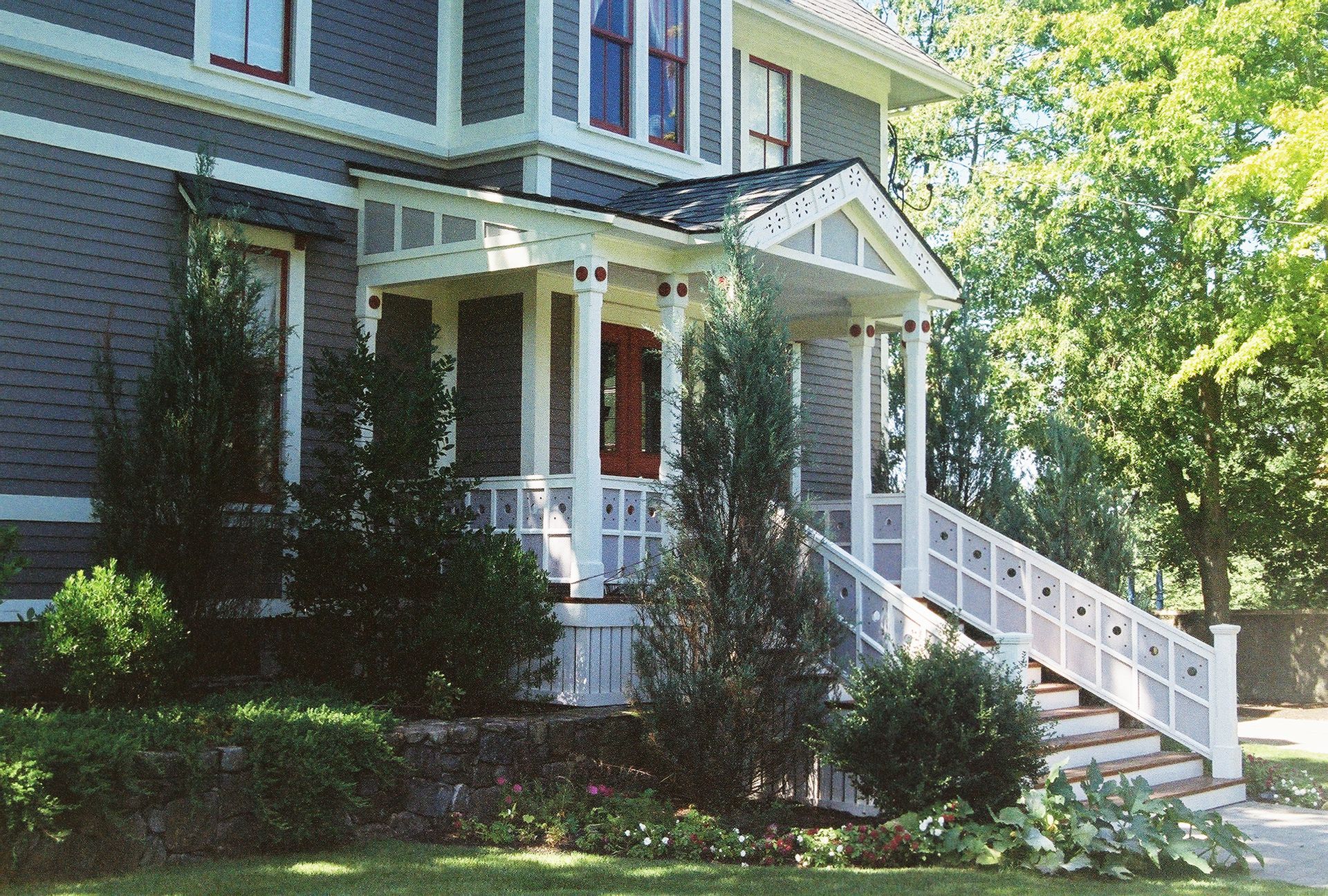 Gray house with white porch, stairs, and columns; red front door.