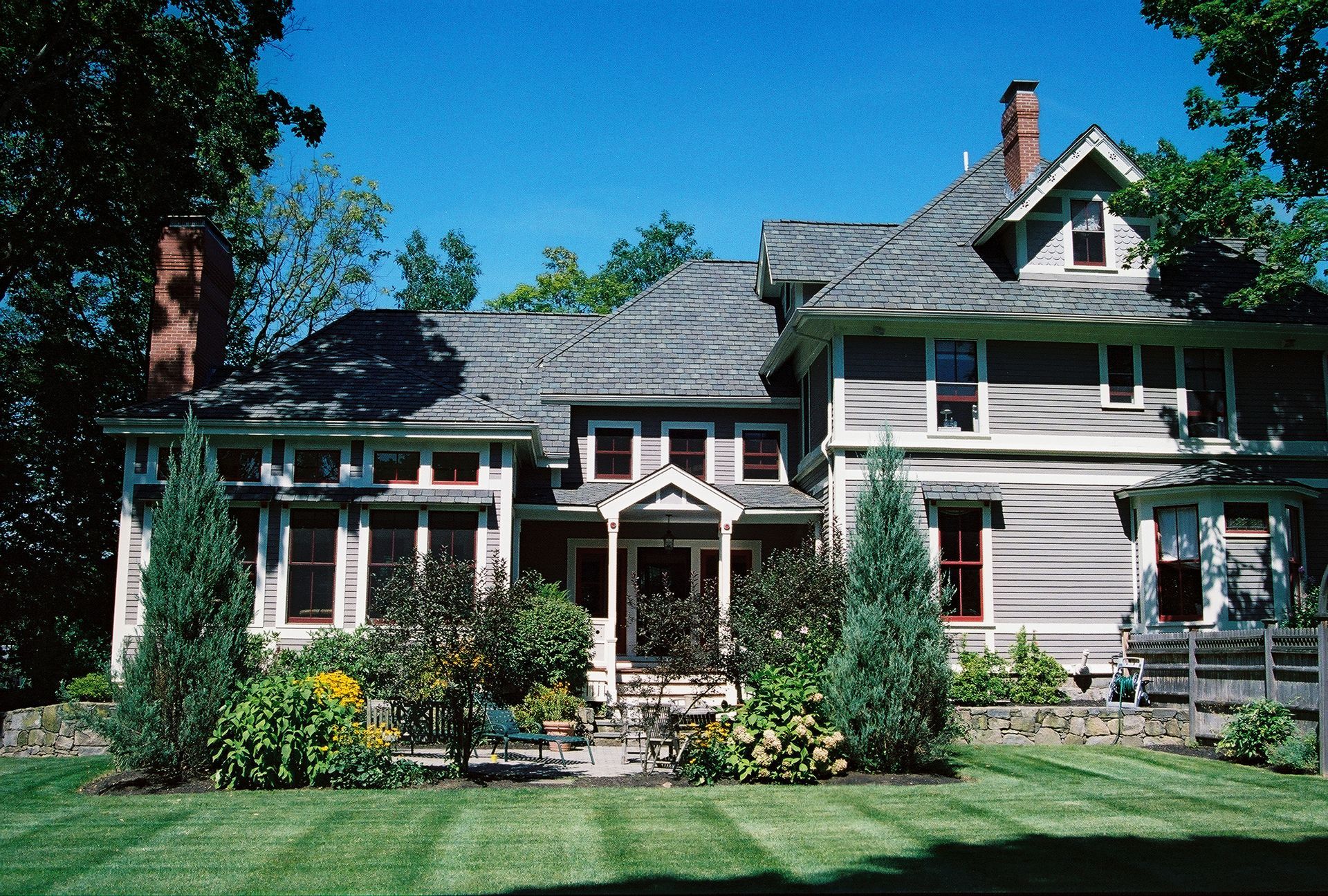 Large two-story house with light brown siding, a grey roof, and a lush green lawn.