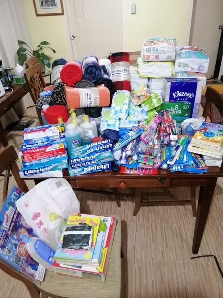 Table piled with donated supplies: blankets, diapers, toiletries, books.