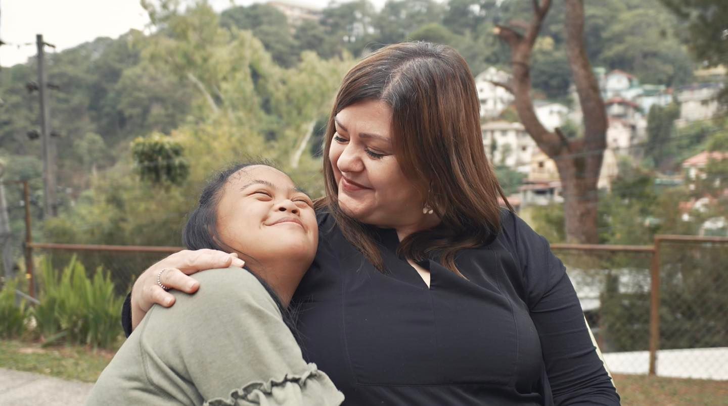 Woman embracing a person with a disability outdoors, both smiling.