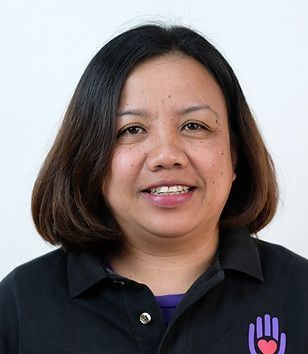 Woman with short dark hair smiling, wearing a black shirt and braces, with a white background.