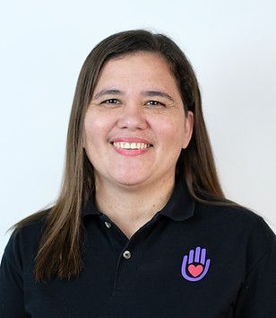 Woman with long brown hair, smiling, wearing a black polo shirt with a purple hand and heart logo.