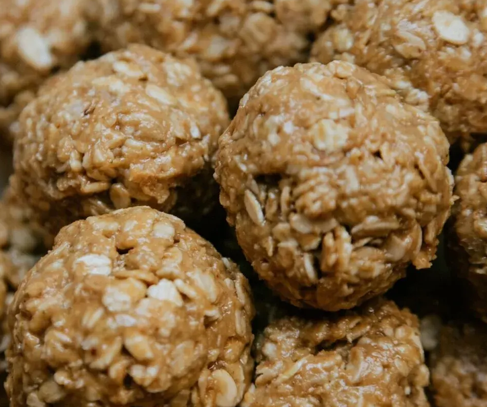 A close-up of a stack of round, tan, textured peanut butter and oat energy bites.