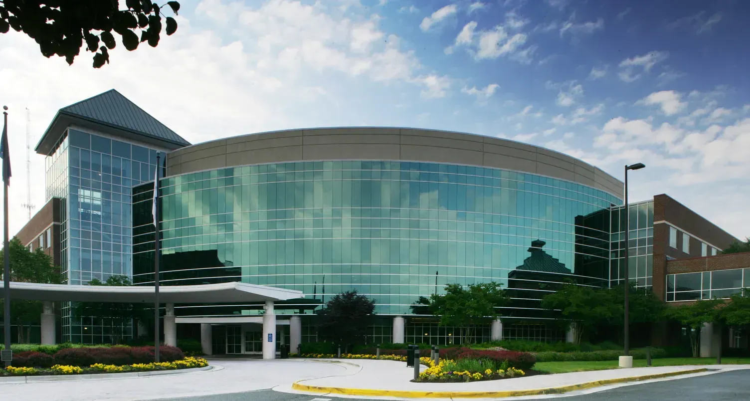 A modern medical building with a prominent curved glass facade, brick wings, a metal roof, and a front driveway entrance.