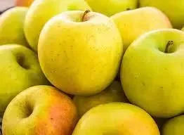 A cluster of vibrant yellow and light green apples with smooth, rounded surfaces filling the frame.