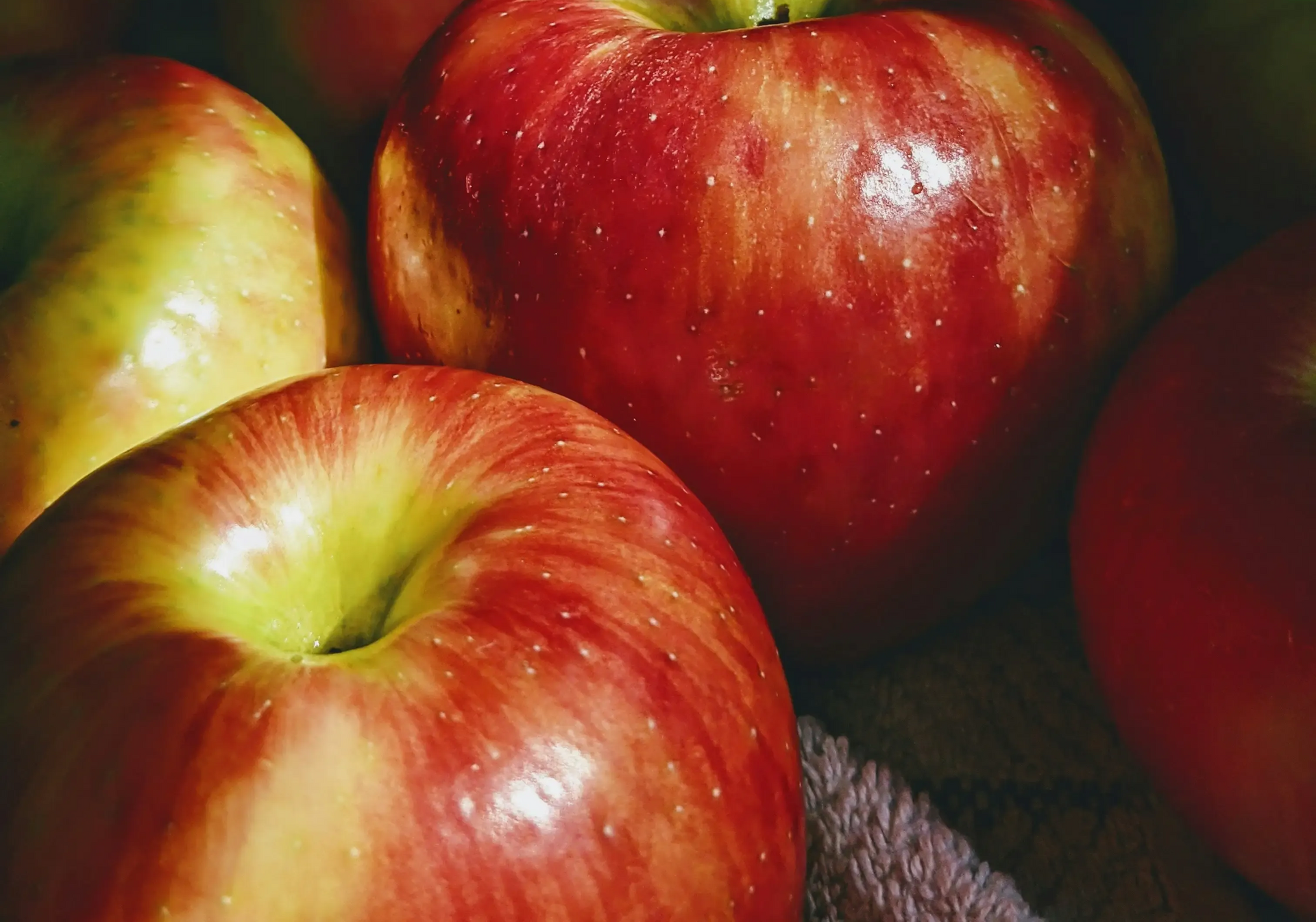 Close-up view of several fresh, shiny red apples with yellow undertones, arranged in a group.