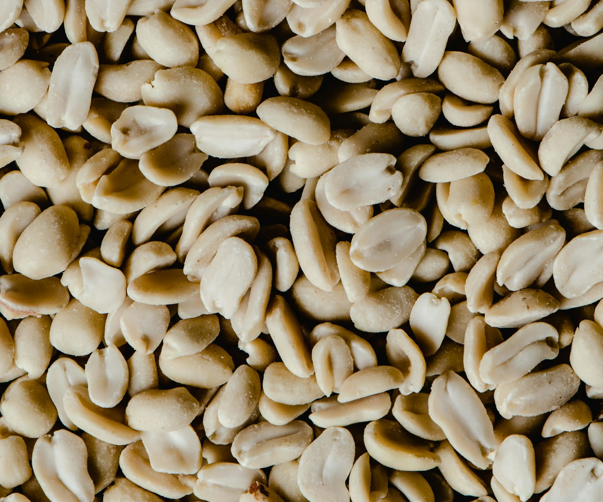 A close-up, high-angle view of a pile of raw, peeled, light beige peanuts.