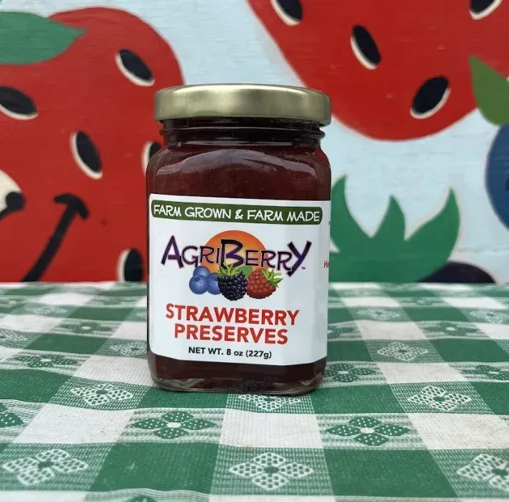 A jar of AgriBerry Strawberry Preserves sits on a green and white checkered tablecloth in front of a painted mural.