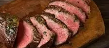 Slices of herb-crusted, medium-rare beef arranged on a wooden cutting board.