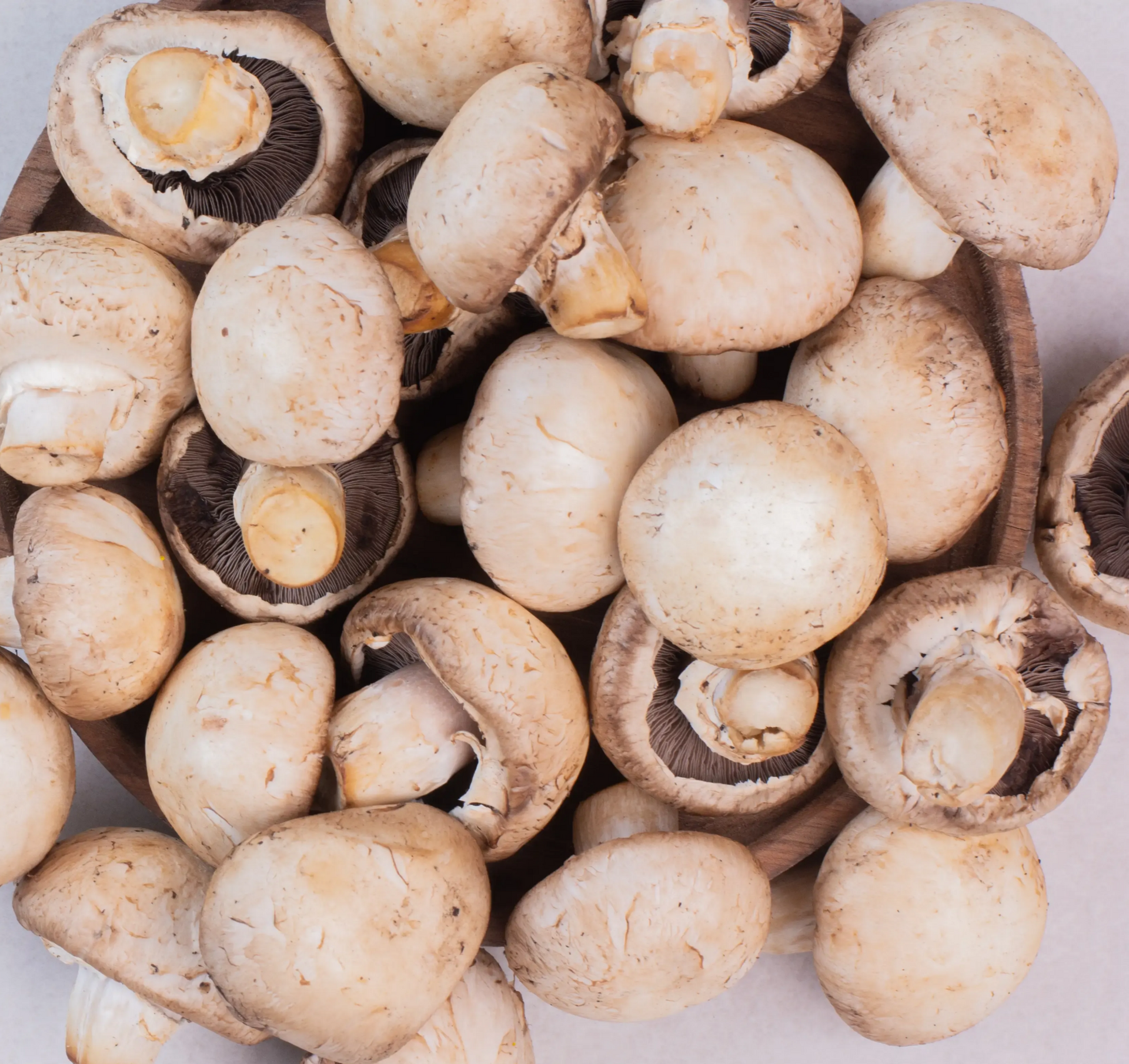 A wooden bowl filled with fresh, whole brown cremini mushrooms.