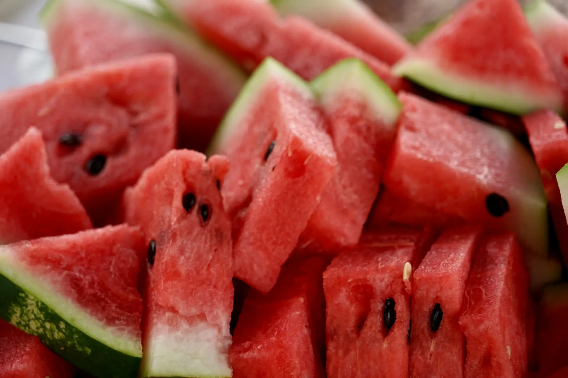 A close-up view of freshly cut, vibrant red watermelon slices with small black seeds and green rinds.