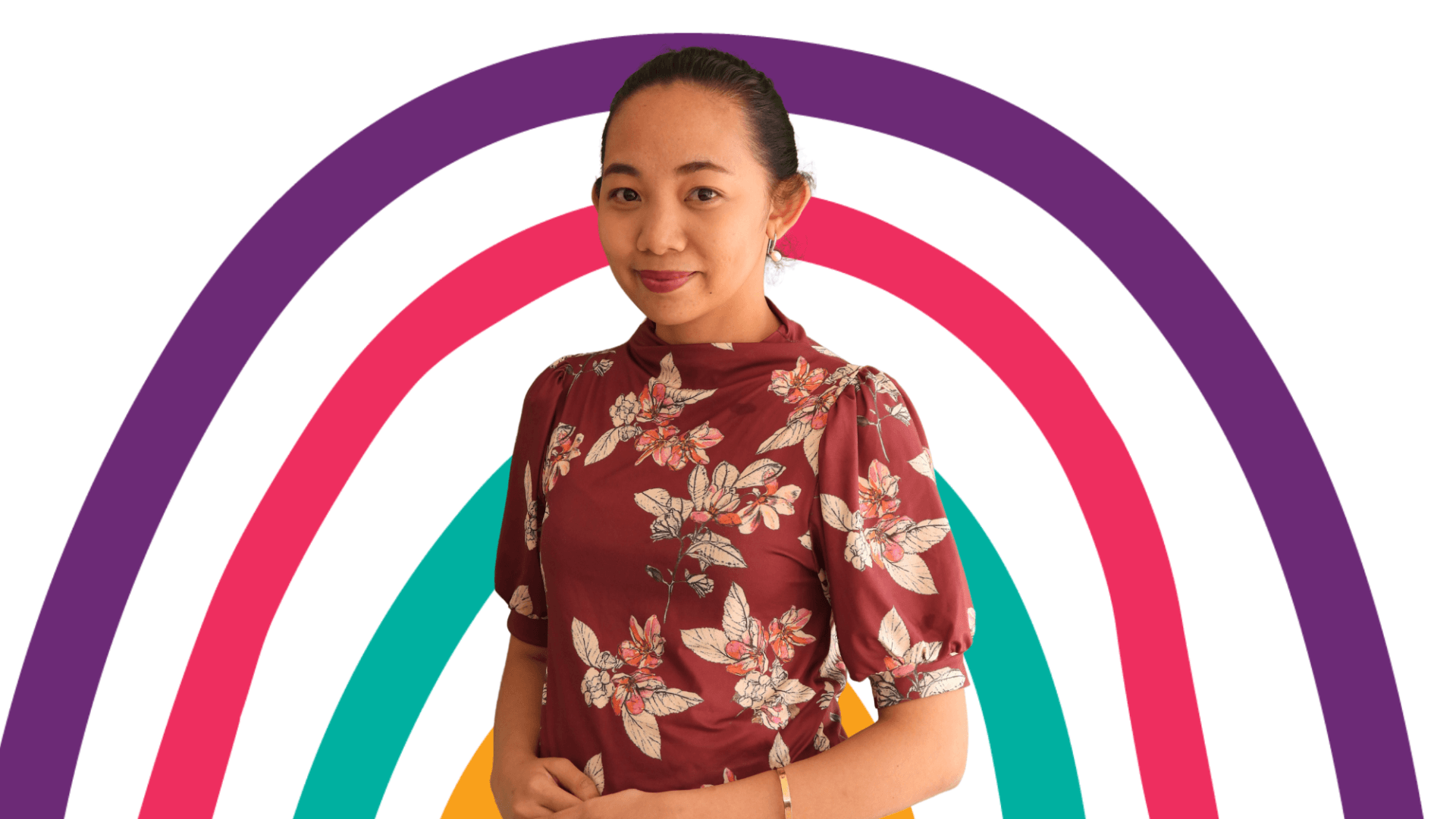A woman in a floral shirt is standing in front of a rainbow.