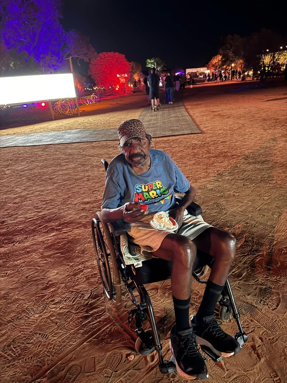 A man is sitting in a wheelchair in a field at night.