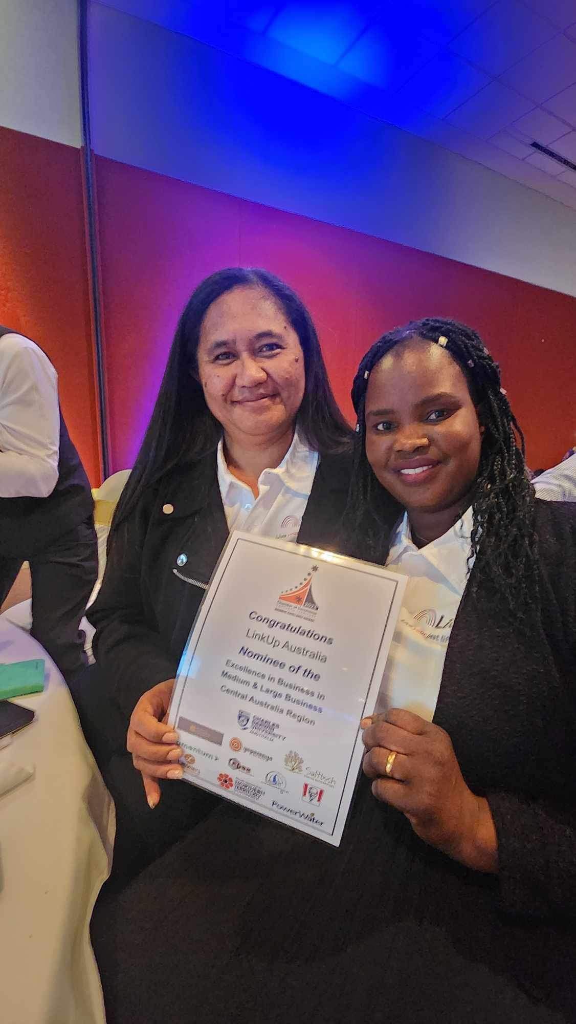Two women are sitting next to each other holding a certificate.