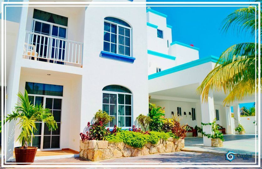 White hotel with blue accents, palm trees, and lush landscaping under a bright blue sky.