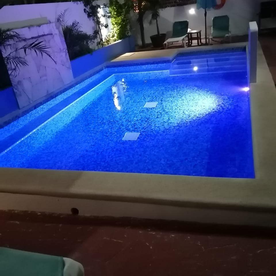 Pool illuminated with blue lights, small seating area, tropical setting.