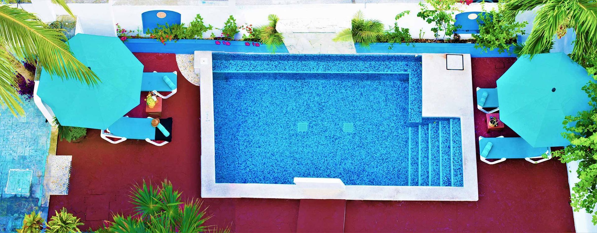 Overhead view of a swimming pool with turquoise umbrellas, surrounded by red pavement and greenery.