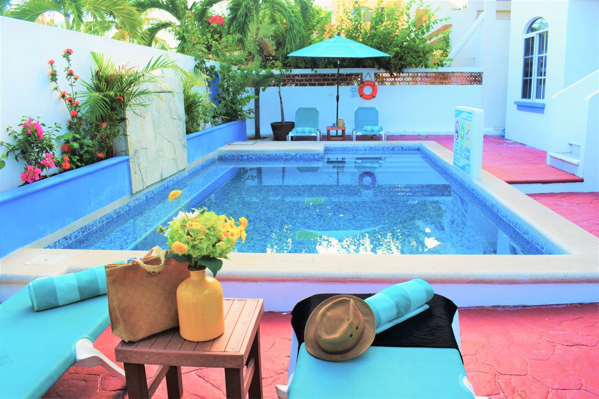 Piscina rodeada de tumbonas, flores y una sombrilla.