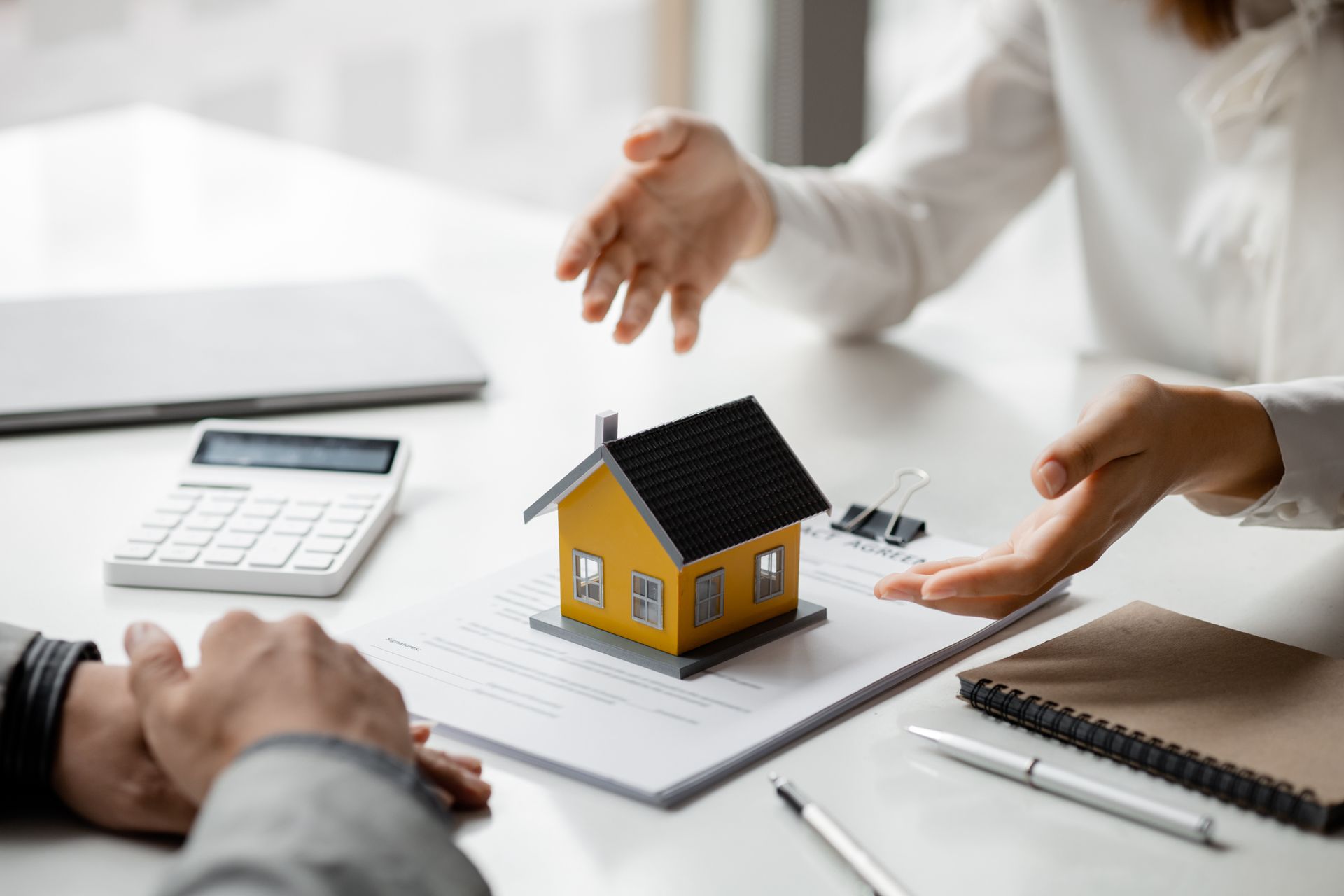 A woman is pointing at a model house on a piece of paper.