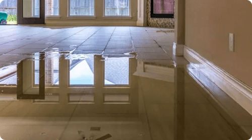 A flooded floor in a living room with water coming out of the windows.