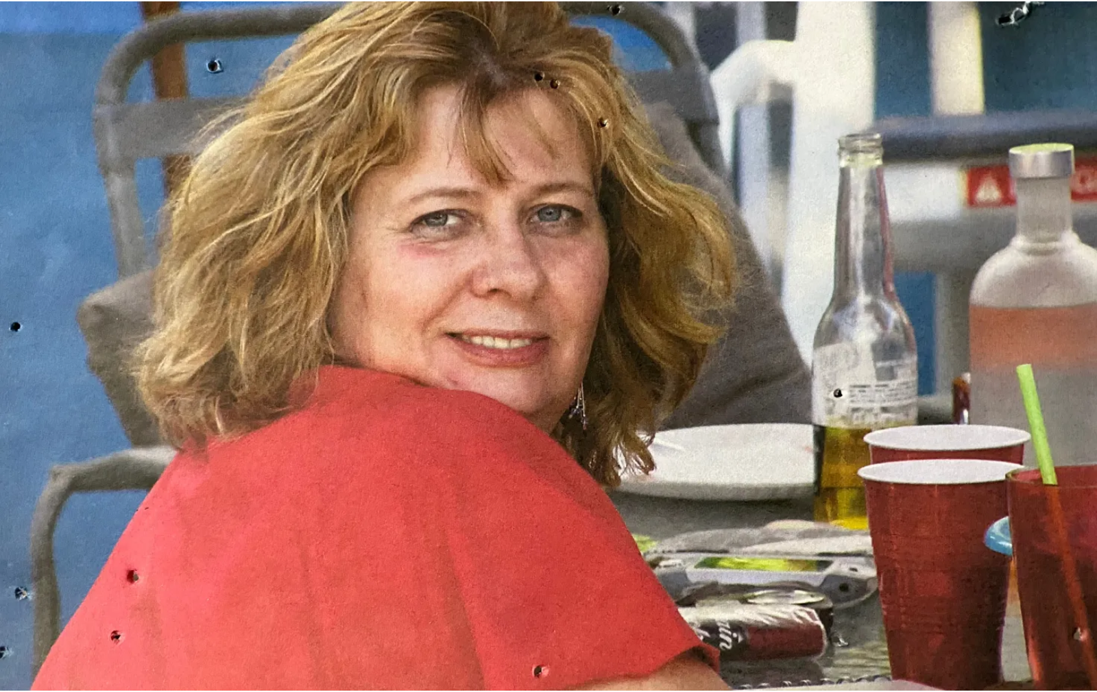 A woman in a red shirt is sitting at a table with cups and bottles