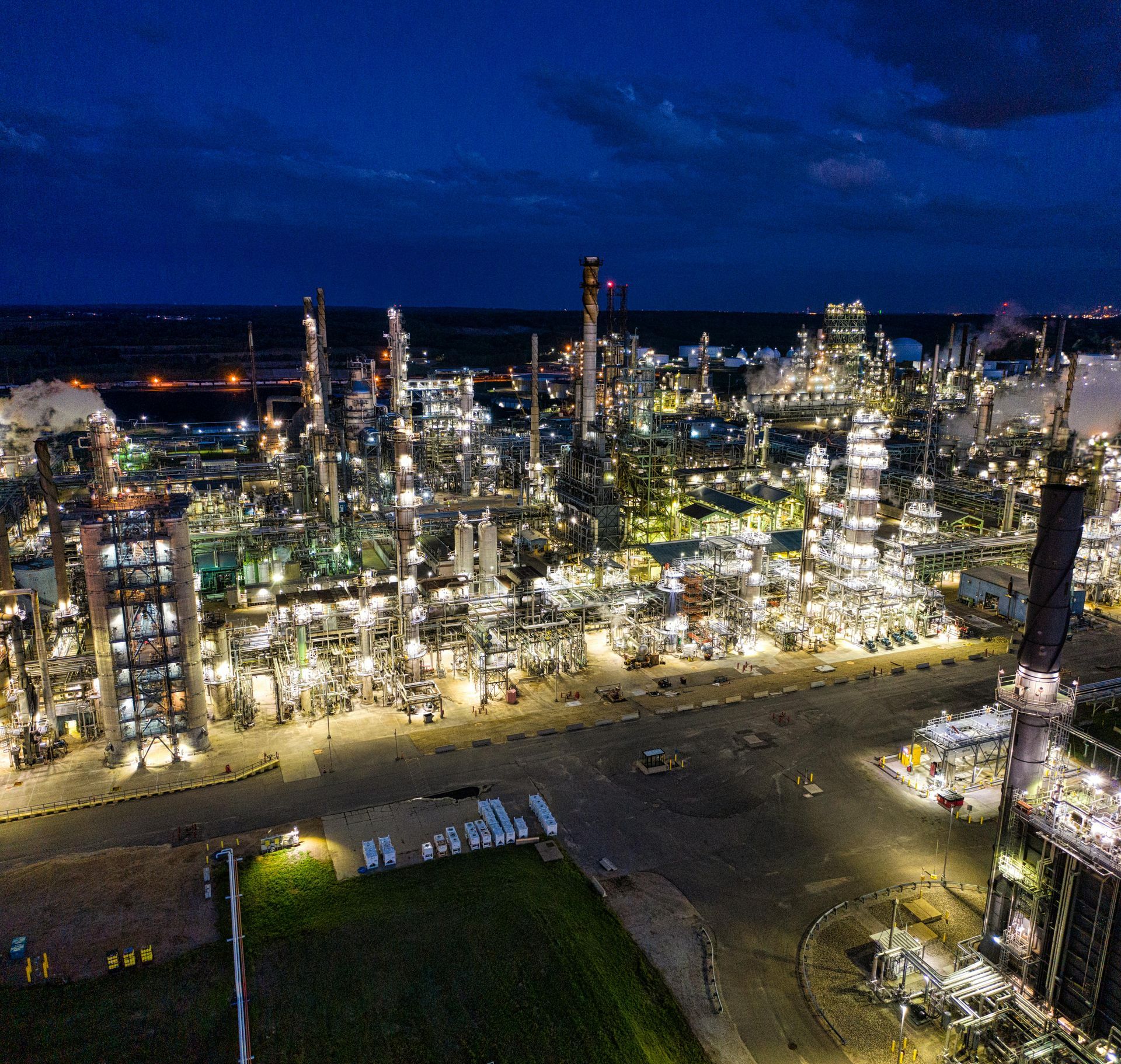 Nighttime industrial refinery glowing with lights under a dark blue sky