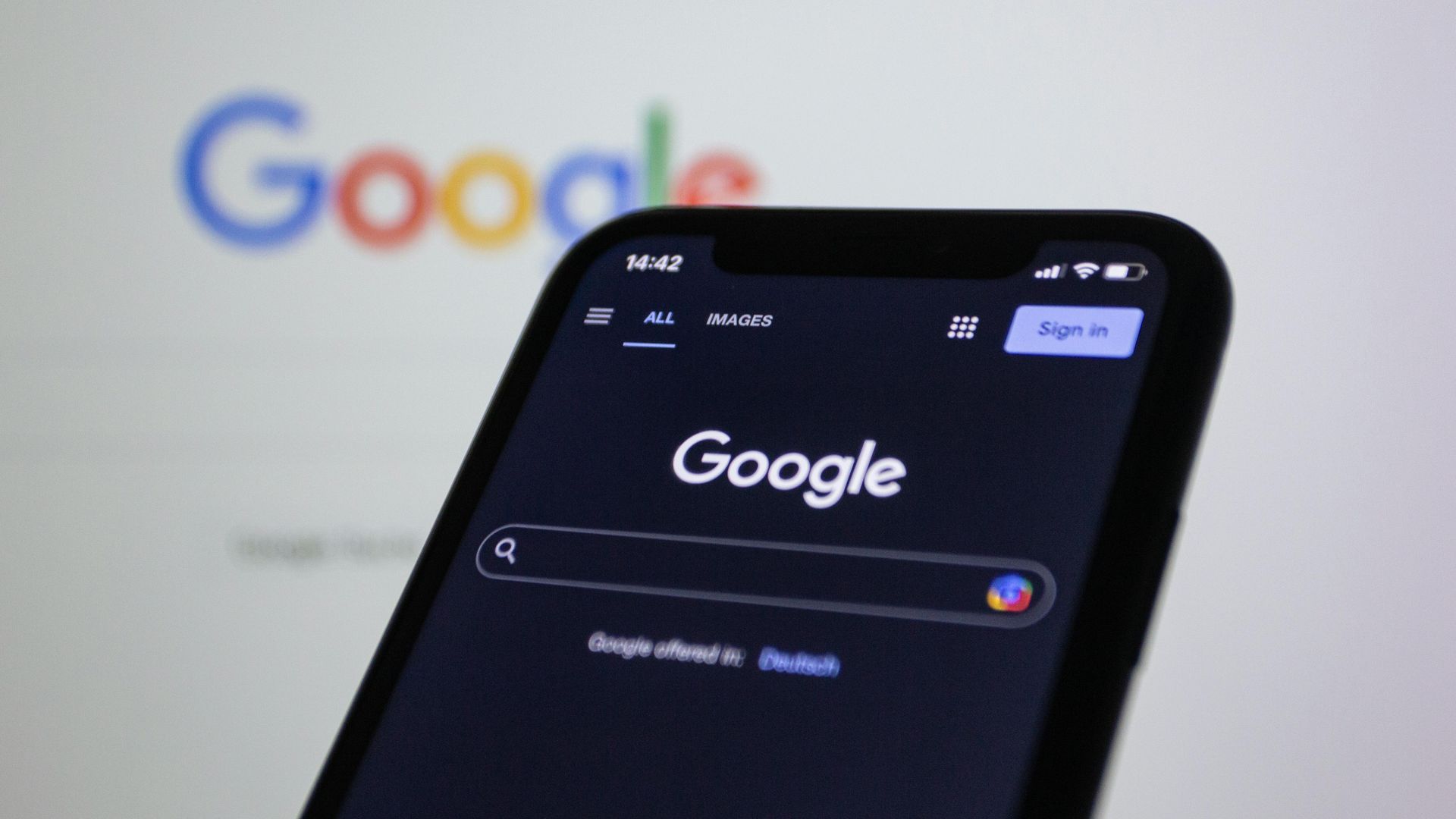 Smartphone showing Google Search page in dark mode, with blurred Google logo in background.