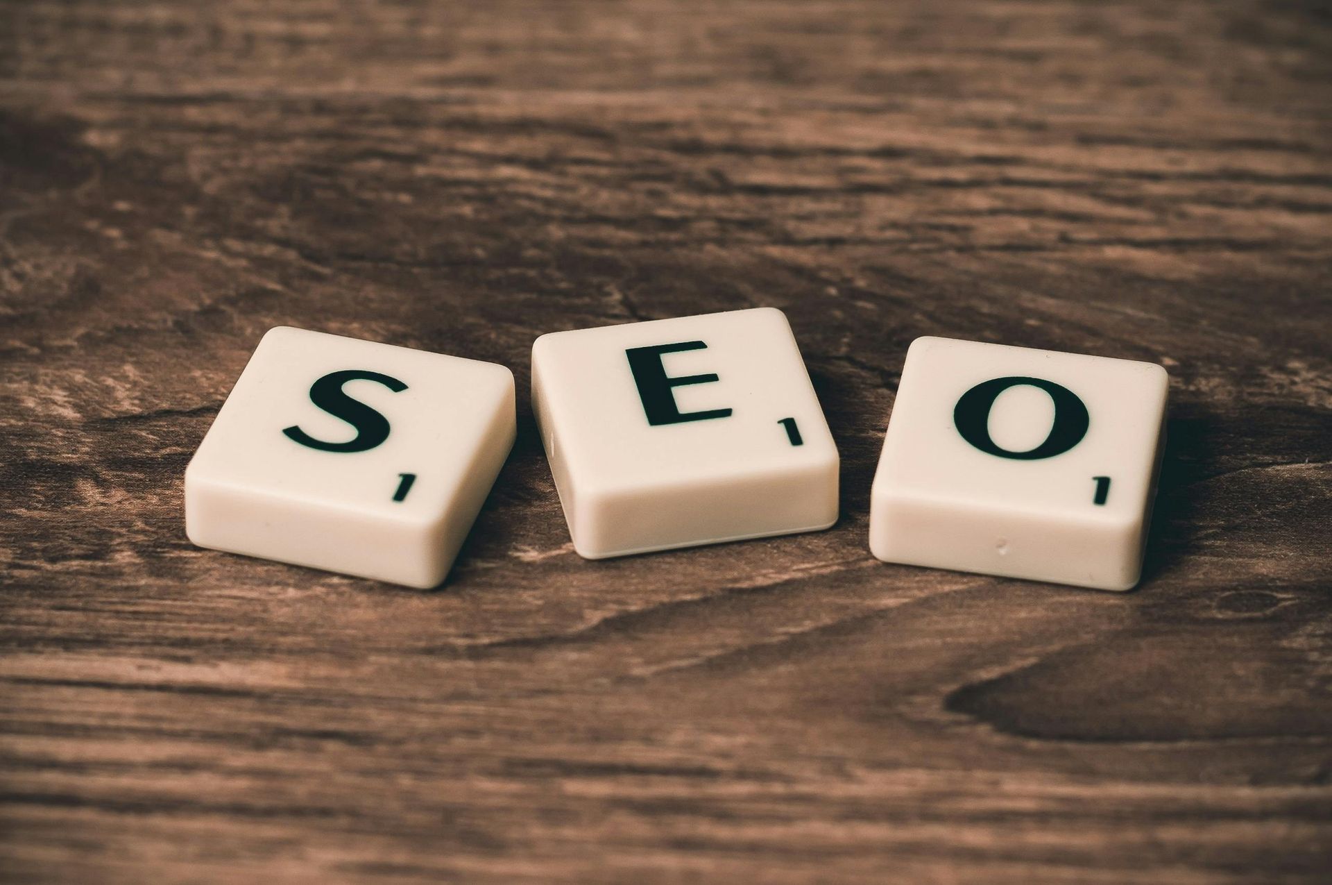 Three white letter tiles spelling SEO on a wooden surface.