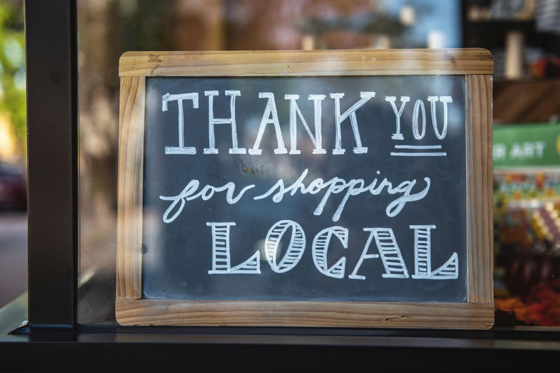 Chalkboard sign reading “Thank you for shopping local” in white lettering on a wooden frame