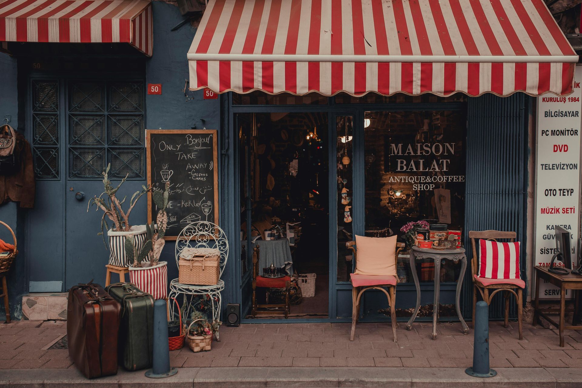 Vintage storefront with red-and-white awning, café chairs, chalkboard sign, and stacked suitcases on the sidewalk