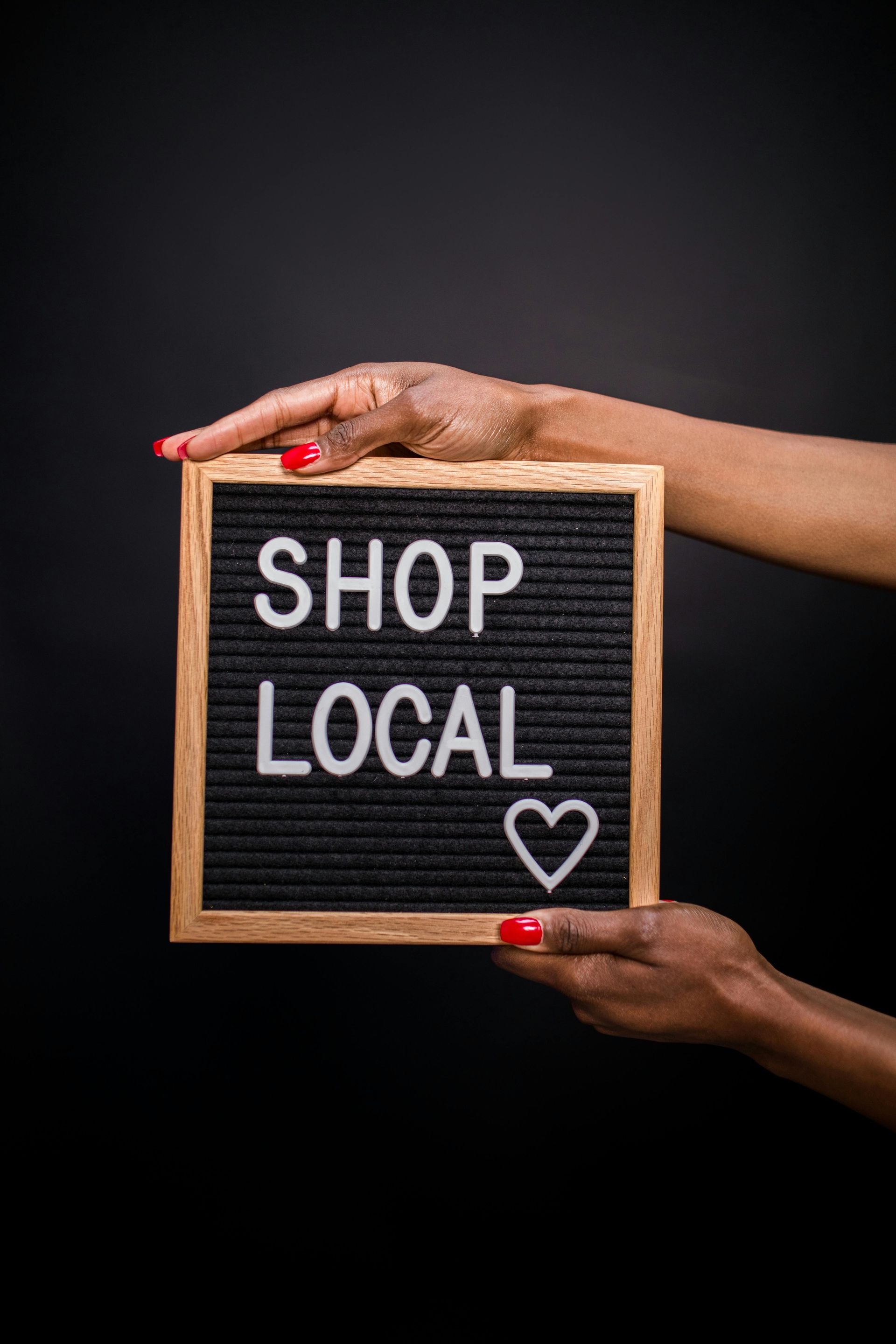 Hands holding a small chalkboard sign reading “SHOP LOCAL” with a heart on a dark background