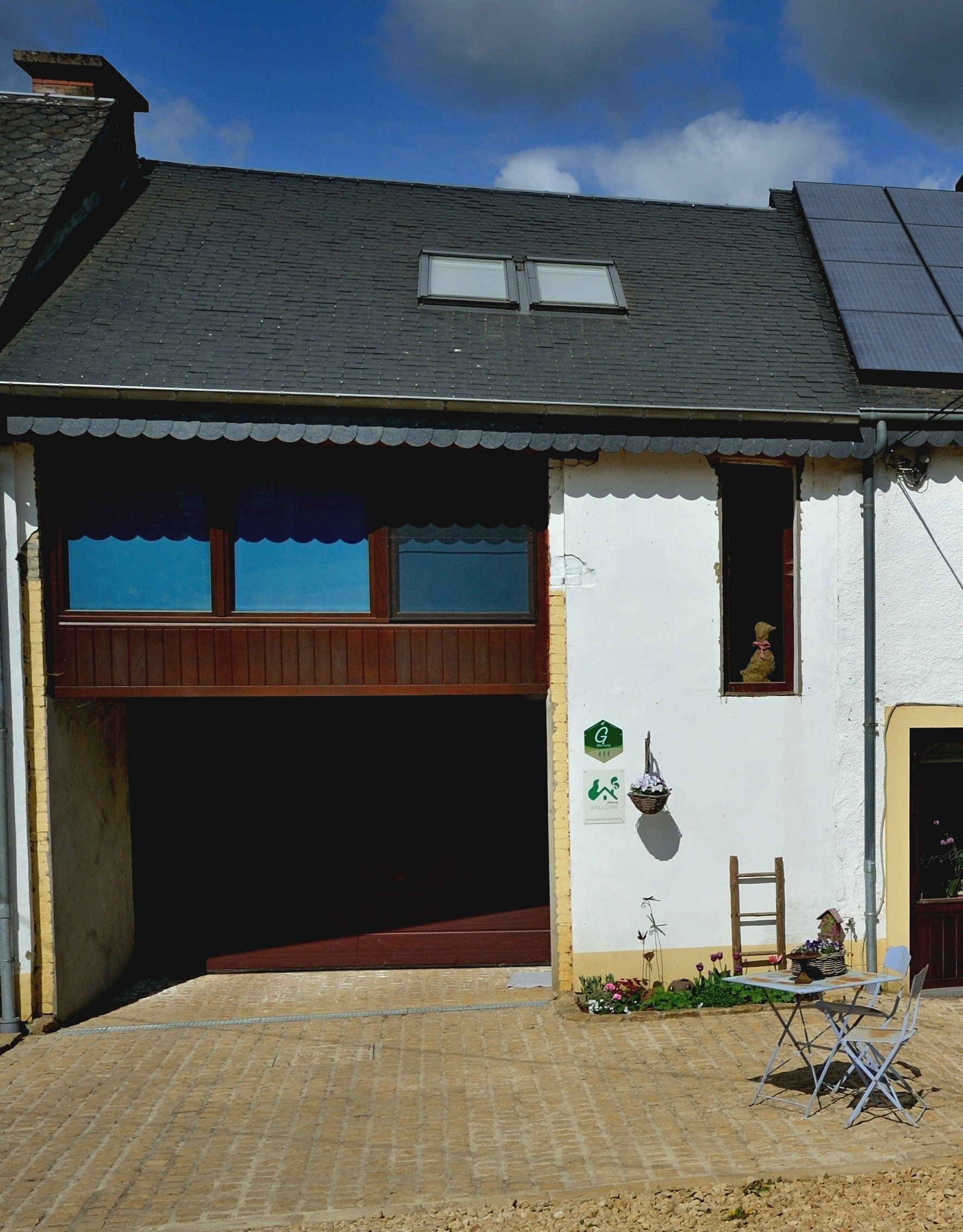 Une maison blanche avec un toit noir a une échelle et des chaises devant elle