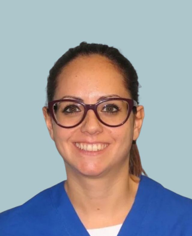 Una donna con gli occhiali e un camice blu sorride alla telecamera