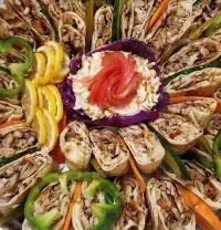 Assorted stuffed wraps arranged in a circular platter, garnished with colorful peppers and herbs.