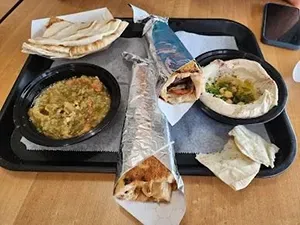 Fast-food tray with wraps, pita bread, and two side dishes on a table