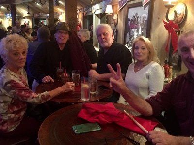 People at a bar, with drinks on a table. One person is giving a peace sign.