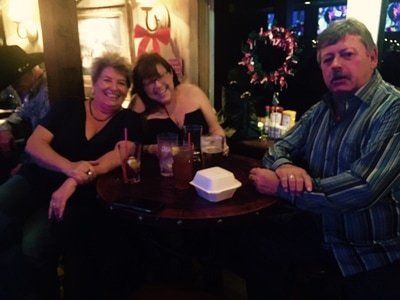 Three people at a dimly lit bar, smiling, around a round table with drinks.