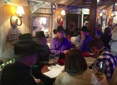 People in cowboy hats at a table in a rustic-themed restaurant. Some are drinking wine.