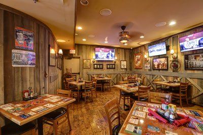 Interior of a rustic restaurant with wood paneling, tables, chairs, and TVs.