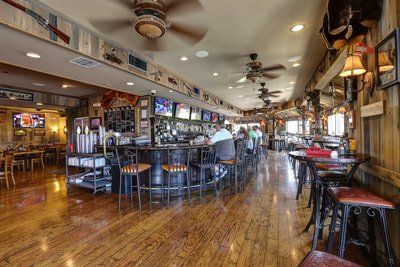 Bar interior with wooden floors and walls, bar stools at a dark wood bar, and televisions.