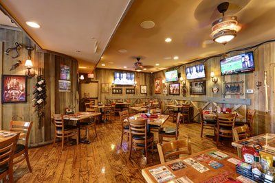 A rustic restaurant interior with wooden walls and floors, tables, chairs, and TVs.