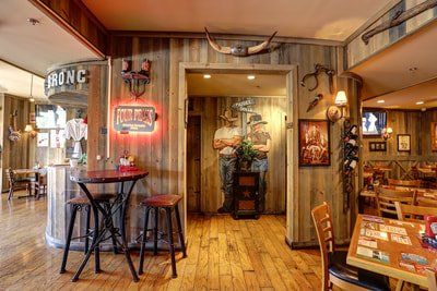 Western-themed restaurant interior with wooden paneling, tables, chairs, and cowboy decor.