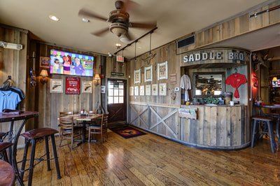 Rustic interior of Saddle Bro, with wooden walls, bar, tables, and ceiling fan.