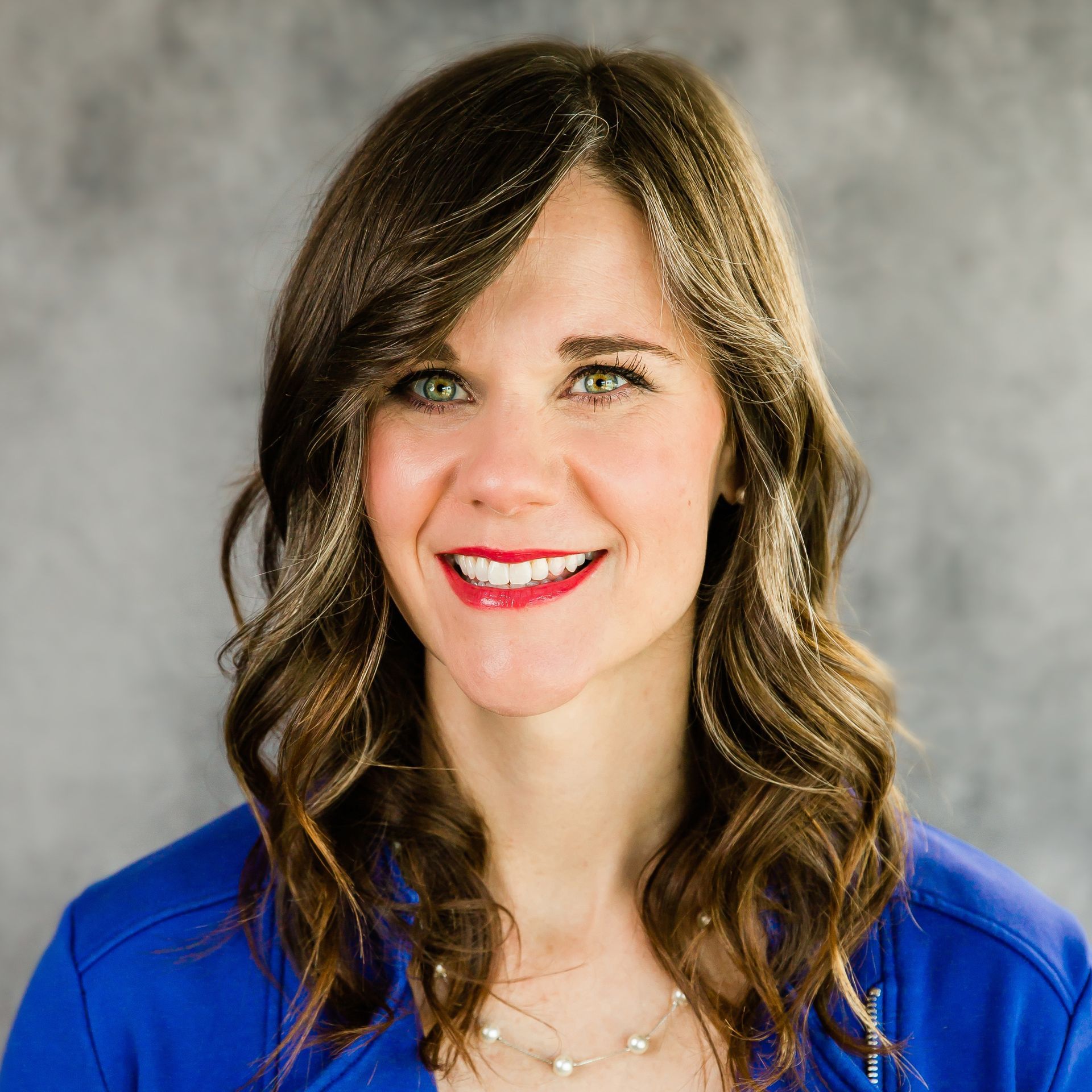 A woman wearing a blue jacket and a necklace is smiling for the camera.