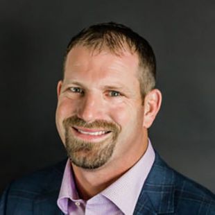 A man with a beard is wearing a suit and smiling for the camera.