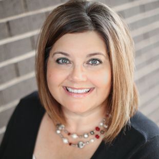 A woman wearing a black jacket and a necklace is smiling for the camera.