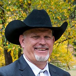 A man in a suit and tie is wearing a cowboy hat and smiling.