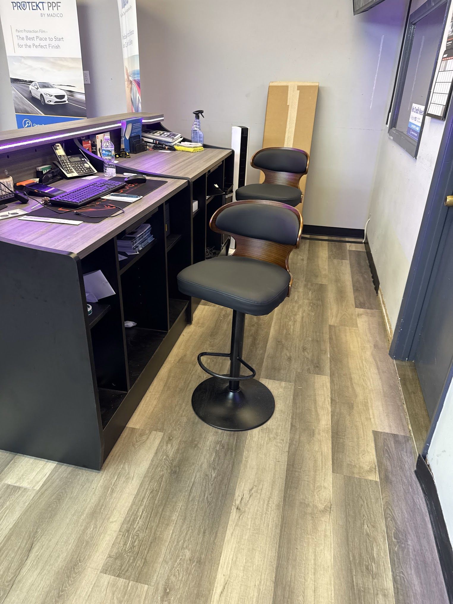 A reception area with a dark desk, two black adjustable stools, and wood-look flooring.
