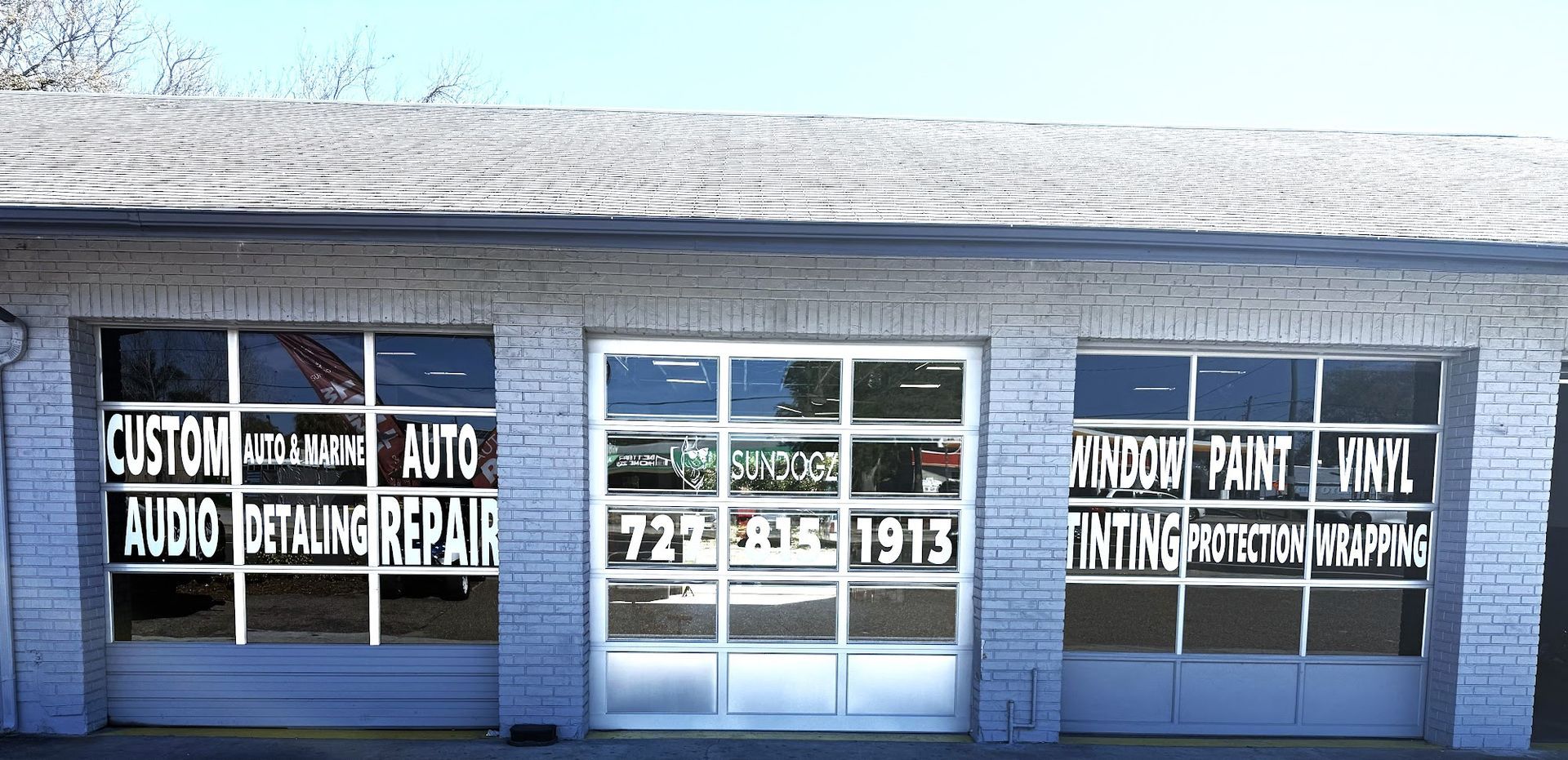 Garage storefront with text on windows, advertising services like custom audio and auto repair. Phone number 727-836-1913.